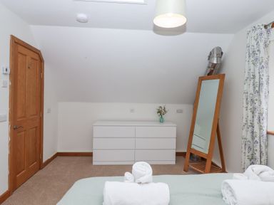 A bedroom with a wooden door a white dresser with a vase and a leaning mirror next to floral curtains at The Old Coach House in Little Dunley Cottages near Bovey Tracey
