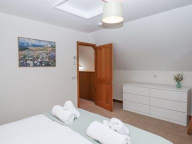 A bedroom with a bed with rolled towels a wooden door a white dresser and a painting on the wall at The Old Coach House Little Dunley Cottages near Bovey Tracey