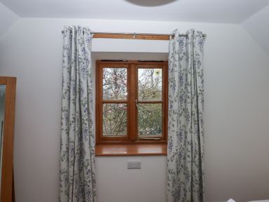 A wooden framed window with floral curtains and a view of blooming trees at The Old Coach House in Little Dunley Cottages near Bovey Tracey