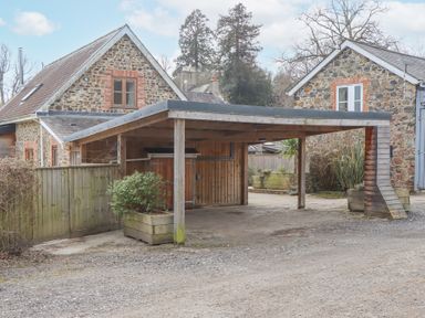 An outdoor carport with wooden posts and a gravel driveway next to stone houses at The Old Coach House in Little Dunley Cottages near Bovey Tracey