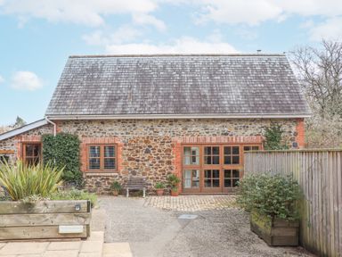 Exterior view of a stone house with wooden windows and doors a bench and plants in pots outside at The Old Coach House in Little Dunley Cottages near Bovey Tracey
