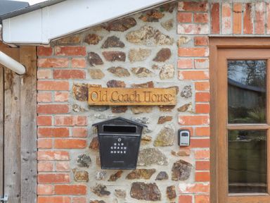 A brick and stone wall with a wooden sign saying Old Coach House a black mailbox and part of a wooden door at The Old Coach House in Little Dunley Cottages near Bovey Tracey