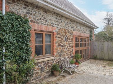 A stone exterior wall with wooden windows and a bench near potted plants at The Old Coach House Little Dunley Cottages near Bovey Tracey