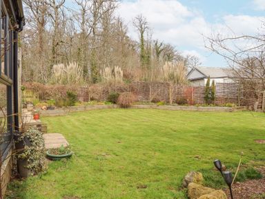 A garden with a lawn bordered by a wooden fence and various plants at The Old Coach House in Little Dunley Cottages near Bovey Tracey