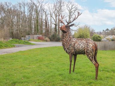A metal sculpture of a stag on grass with trees and buildings in the background at The Old Coach House in Little Dunley Cottages near Bovey Tracey
