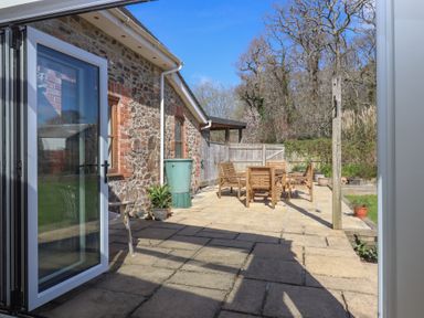 An outdoor patio area with wooden chairs and table beside a stone wall house at The Old Coach House Little Dunley Cottages near Bovey Tracey