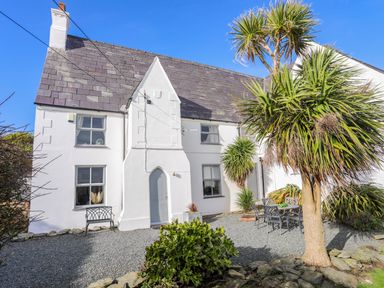 A white house with slate roof and gravel yard with chairs and table at School House in Aberffraw