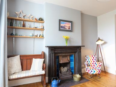 A sitting area with a wooden bench, a fireplace with blue tiles, a colorful armchair, and a floor lamp at School House in Aberffraw