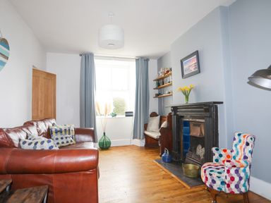 A living room with a leather sofa a colorful chair and a fireplace at School House in Aberffraw