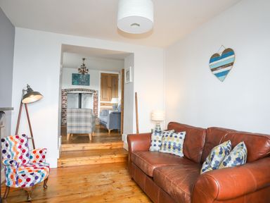 A living room with a leather sofa and patterned armchair by a standing lamp leading to another room with armchairs at School House in Aberffraw