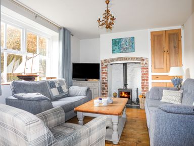 A living room with blue sofas a wooden coffee table a fireplace and a television at School House in Aberffraw