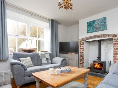 A living room with blue sofas a wooden coffee table and a wood burning stove at School House in Aberffraw