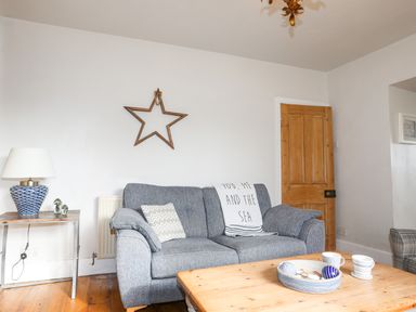 A living room with a gray sofa pillows wooden star wall decor wooden door and a side table with lamp at School House in Aberffraw