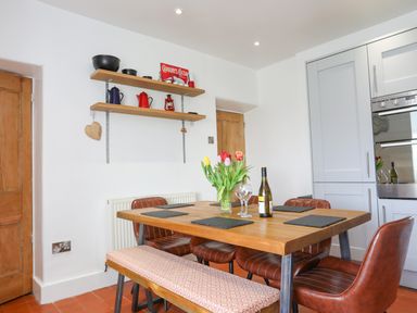 A dining area with a wooden table set with a wine bottle and glasses surrounded by chairs and a bench in a kitchen at School House Aberffraw