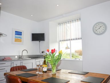 A kitchen with a wooden dining table with a vase of flowers wine glasses and placemats at School House in Aberffraw
