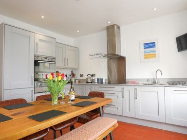 A kitchen with a wooden dining table with black placemats and a vase of tulips a countertop with a kettle built-in oven and a stainless steel extractor hood at School House in Aberffraw