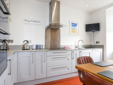A kitchen with white cabinets a stainless steel range hood a kettle and a sink with a faucet at School House in Aberffraw