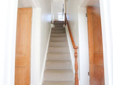 A carpeted staircase with wooden handrail between two wooden doors at School House in Aberffraw