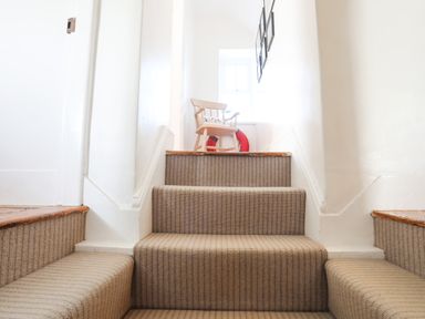 Carpeted staircase leading up to a small landing with a wooden chair and a red lifebuoy at School House in Aberffraw