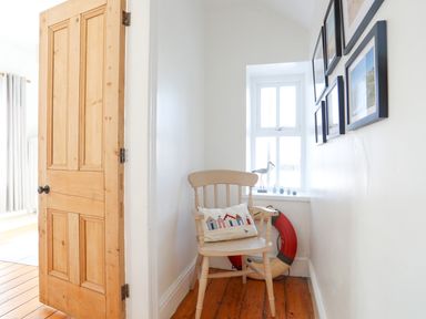 A wooden chair with a decorative pillow and a life ring near a window in a hallway at School House in Aberffraw