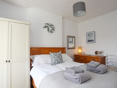 A bedroom with a wooden bed with white bedding and folded towels on top next to a white wardrobe and wooden dresser at School House in Aberffraw
