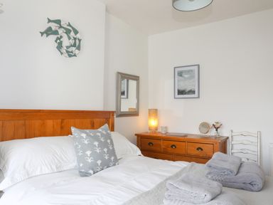 A bedroom with a wooden bed frame white bedding a dresser with a lamp and a chair at School House in Aberffraw