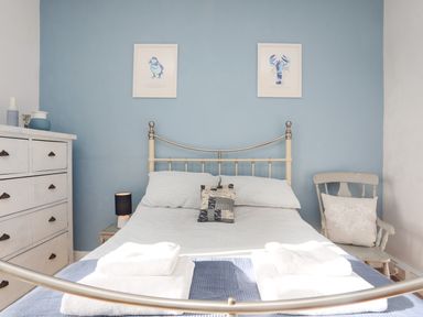 A bedroom with a metal bed frame blue wall white dresser chair and framed bird and lobster prints at School House in Aberffraw
