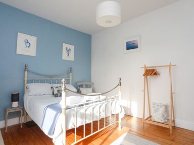 A bedroom with a metal bed white bedding and blue wall art at School House in Aberffraw