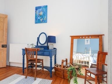 A bedroom with a blue dressing table and wooden chairs next to a large mirror and a basket with branches and plants at School House in Aberffraw