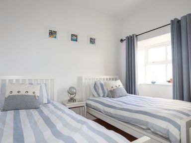 A bedroom with two single beds striped bedding a small table with a lamp and framed pictures on the wall at School House in Aberffraw