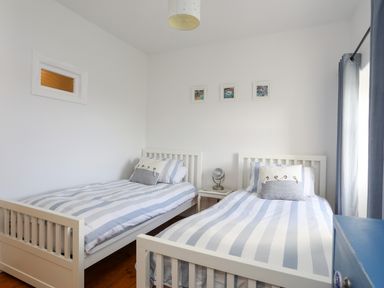 A bedroom with two single beds with striped bedding a small table with a lamp between the beds and blue curtains at School House in Aberffraw