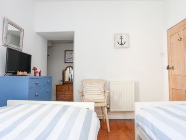 A bedroom with two single beds with striped bedding a blue dresser with a TV a wooden chair with a pillow and a wooden door at School House in Aberffraw