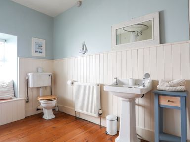 A bathroom with a toilet a pedestal sink a mirror towels on a small table and wooden floor at School House in Aberffraw