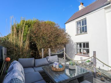 An outdoor seating area with a glass table and cushioned chairs near a white house at School House in Aberffraw
