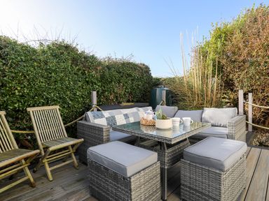 An outdoor patio with rattan furniture and wooden chairs surrounded by greenery at School House in Aberffraw