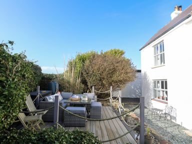 An outdoor deck with wicker seating and a wooden chair next to a white house at School House in Aberffraw