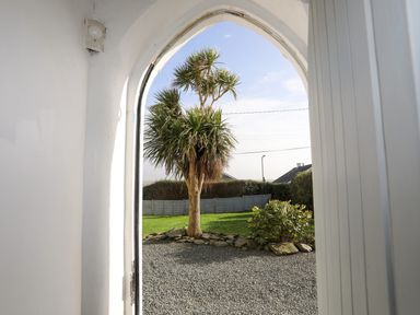 A view through an arched doorway showing a gravel area, a tree, a lawn, and a fence at School House in Aberffraw
