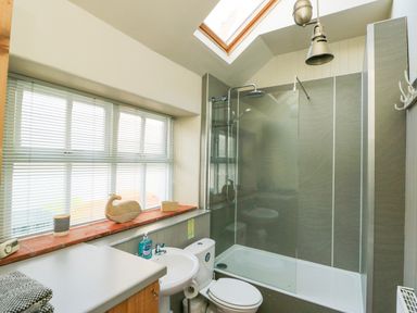 A bathroom with a shower bathtub toilet sink and window at School House in Aberffraw
