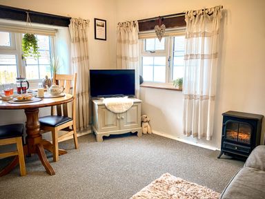 A living room with a round wooden table set for tea two wooden chairs a television on a cabinet and a small stove at Hawthorn in Crackington near Crackington Haven