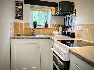 A kitchen sink with utensils hanging and a stove next to a window at Hawthorn Crackington near Crackington Haven