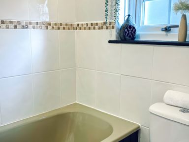 A bathroom corner with a bathtub a window with decor and a toilet with a rolled towel at Hawthorn in Crackington near Crackington Haven