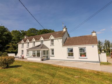 A two-story white farmhouse with a brown tiled roof and porch surrounded by grass at Dromclough Farmhouse in Dromclough near Listowel County Kerry