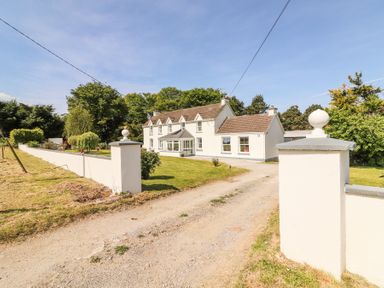 A farmhouse with a gravel driveway and white boundary wall surrounded by trees and grass at Dromclough Farmhouse in Dromclough near Listowel County Kerry
