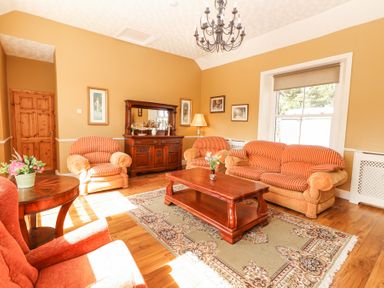 A living room with orange striped sofas a wooden coffee table and sideboard a patterned rug and a chandelier at Dromclough Farmhouse in Dromclough near Listowel County Kerry