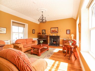 A living room with sofas, a fireplace, a piano, a coffee table, paintings on walls, and wooden flooring at Dromclough Farmhouse in Dromclough near Listowel County Kerry