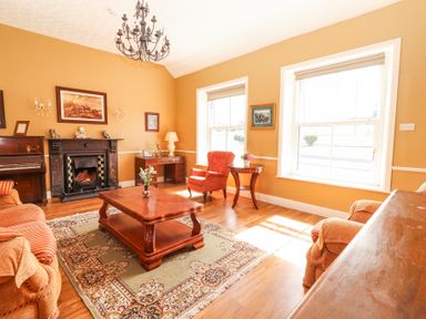 A living room with a wooden coffee table sofa armchair desk piano and fireplace at Dromclough Farmhouse in Dromclough near Listowel County Kerry