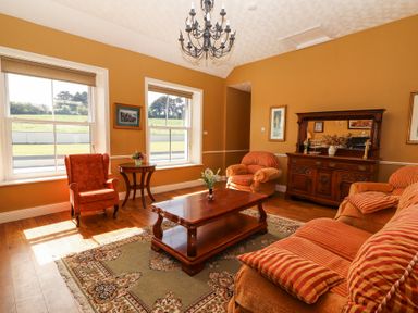 A living room with armchairs a wooden coffee table and a sideboard with a mirror at Dromclough Farmhouse in Dromclough near Listowel County Kerry