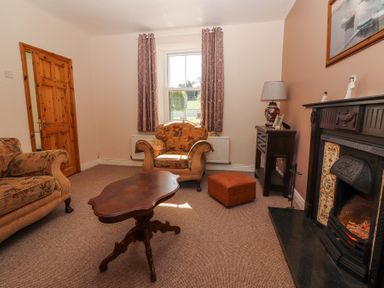 A living room with armchairs a wooden coffee table a fireplace and a side table with a lamp at Dromclough Farmhouse in Dromclough near Listowel County Kerry