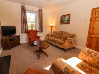 A living room with floral patterned sofas an orange armchair wooden coffee table and a TV on a wooden cabinet at Dromclough Farmhouse in Dromclough near Listowel County Kerry