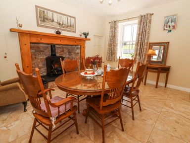 A dining room with wooden chairs a glass top table and a fireplace at Dromclough Farmhouse in Dromclough near Listowel County Kerry